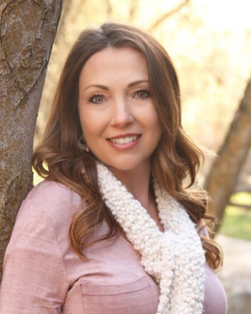 Char, smiling, photographed outdoors beside a tree.