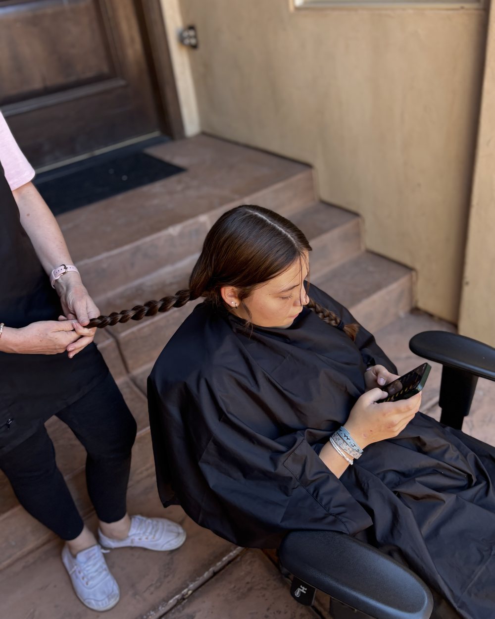 Holding out a finished braid, ready to be cut off, on the front steps.
