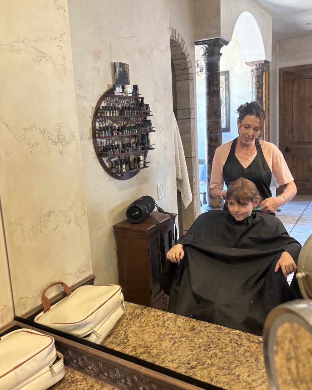 Combing out a young client's hair at a mirror, reflected in the glass.